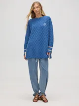 Sweater color crema con tejido en ochos, cuello redondo, puños acanalados con doble raya azul y tajos a los costados.