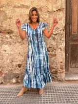 Vestido largo con estampado tie-dye en tonos azules y blancos, con mangas cortas con volados y falda con volados en el ruedo.