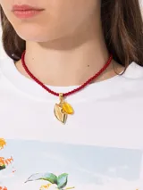 Collar corto de cuentas rojas con dije dorado en forma de hoja y dije de cristal amarillo.