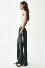 Pantalón negro de tiro alto con cintura elástica, bolsillos delanteros y detalle de banda lateral blanca.