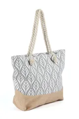 Bolso tipo tote playero con cuerpo estampado en patrón de hojas estilizadas en gris y blanco, y base de arpillera color beige. Las asas son de cuerda gruesa trenzada de color crudo.