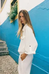 Camisa blanca de manga corta con cuello solapa, bolsillos frontales con tapeta, bajo con elástico y cierre frontal con botones a presión.
