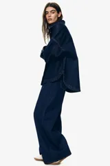 Pantalón de jean azul oscuro de tiro alto, corte recto y pierna ancha. Diseño de cinco bolsillos con costuras a la vista. Inspirado en los años 70.