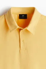 Remera polo de manga corta color amarillo, confeccionada en punto de algodón liviano. Tiene cuello clásico, tapeta con botones y corte ajustado.