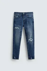 Pantalón de jean azul oscuro con efecto lavado y roturas en las rodillas, de corte ajustado al cuerpo desde la cintura hasta el tobillo.