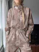 Camisa marrón con estampado de arabescos blancos, de corte holgado, cuello alto con volados y mangas largas.