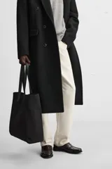 Bolso tipo shopper negro fabricado en tejido de algodón con asas de piel. Cuenta con dos bolsillos laterales exteriores y un bolsillo interno.