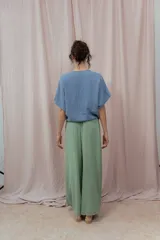 Blusa de lino color azul claro con escote en V cruzado y manga corta. Se ajusta en el centro del busto con un botón redondo de madera o metal con relieve.