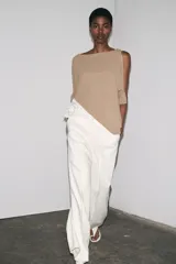 Top color beige de tejido de punto con mangas 3/4 y bajo asimétrico. Detalle de tejido combinado doble capa con encaje blanco en el ruedo.