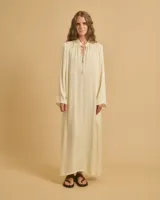 Vestido largo color crema, de corte amplio y mangas largas. Tiene cuello redondo con cordón ajustable.