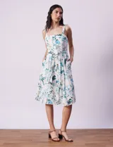 Vestido midi blanco con estampado floral celeste y verde, escote recto con tirantes, abertura frontal con botones, lazo en la cintura y bolsillos laterales.
