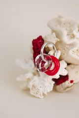 Aros colgantes con aro de acero quirúrgico y dijes circulares de cristal de Murano, uno transparente con inclusiones rojas y otro rojo sólido.