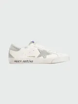 Championes Golden Goose modelo Super Star, de cuero color blanco con detalles en gris, cordones y suela desgastada. Presentan una estrella gris en el lateral y el logo GGDB en la lengüeta.