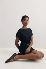 Vestido negro a la rodilla con escote bote y pliegues de caja invertidos adelante y atrás. Modelo de manga corta con cintura entallada, cinturón extraíble con hebilla de metal y bajo recto. Cierre oculto en la espalda. Sin forrar.