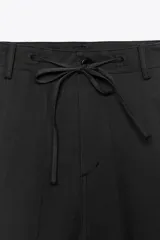 Pantalón cargo negro de corte amplio con cintura ajustable con cordón, bolsillos laterales y bolsillos tipo parche en las piernas.