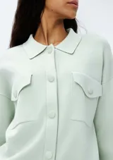 Chaqueta color verde agua con cuello camisero, cierre frontal con botones, dos bolsillos de parche con solapa en el pecho y mangas largas.