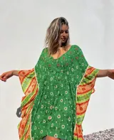 Túnica corta verde con estampado de flores blancas y detalles bordados en el escote. Mangas anchas con terminación en tela estampada a rayas naranjas y blancas.