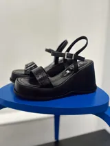 Sandalias negras de plataforma con tira ancha sobre el empeine y pulsera al tobillo con hebilla metálica.