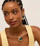 Conjunto de collar tipo gargantilla abierta y aros con tornillo, ambos con colgante y detalle de piedra de resina. El collar es dorado y tiene un dije con una piedra de resina turquesa y detalles en blanco y negro. Los aros son dorados con una piedra de resina turquesa.