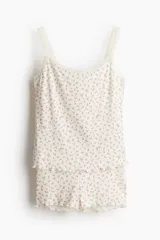 Conjunto de pijama de dos piezas en punto acanalado color blanco con estampado de pequeñas flores rosas. El top es de breteles finos con ribete de encaje en el escote y bajo sobrehilado. El short tiene cintura elástica y bajo sobrehilado.