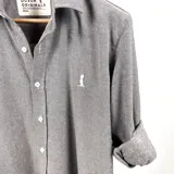 Camisa gris de manga larga con puños enrollados, cuello clásico y cierre con botones.