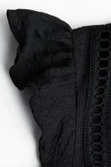 Top negro de manga corta con textura arrugada, escote redondo con abertura en V ajustable con lazos y canesú con inserciones de encaje calado. Corte holgado con costura fruncida bajo el busto.