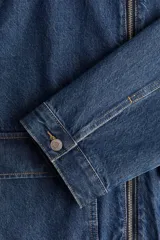 Campera de denim azul con cuello, cierre frontal y canesú en la espalda. Tiene puños abotonados, bolsillos delanteros con solapa y bolsillo interior de parche en el pecho.