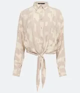 Camisa de crepé color beige con estampado geométrico en tonos neutros, cuello camisero, manga larga y cierre con botones. Tiene un lazo frontal para atar.