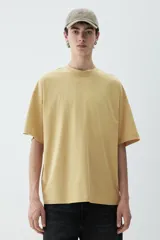 Remera color mostaza de algodón de peso medio, corte oversized, con cuello redondo ribeteado, hombros caídos y bajo recto.