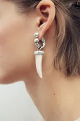 Aros metálicos plateados con colgante de cuerno de resina color crema. Cierre con tuerca.