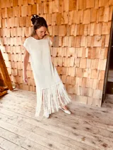 Vestido tejido color blanco con hilo metalizado, corte oversized, mangas cortas y flecos en el ruedo.