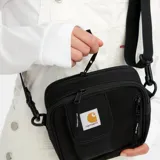 Bandolera Carhartt Work In Progress modelo Essentials Small, color marrón, con correa ajustable negra, bolsillo frontal con solapa y logo bordado.
