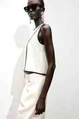 Blusa blanca sin mangas de crepe con cuello redondo y detalle de ribete negro en cuello, sisas y abertura frontal diagonal.