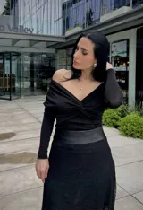 Blusa negra con escote off-shoulder y mangas largas ajustadas.