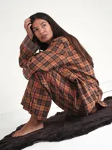 Conjunto de pijama a cuadros color naranja y negro con ribetes rosas. Incluye camisa de manga larga con cuello y pantalón largo de corte recto.