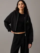 Buzo negro cropped con capucha y cierre frontal de cremallera metálica. Tiene bolsillos de parche en la cintura y logo de Calvin Klein bordado en el pecho.