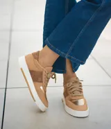 Zapatilla de cuero color tostado con detalles dorados y suela blanca.