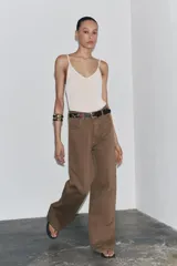 Pantalón de jean color marrón, de tiro alto, corte wide leg y relaxed fit. Cuenta con bolsillos delanteros y traseros, trabillas en la cintura, cierre frontal con cremallera, botón interior y gancho metálico.
