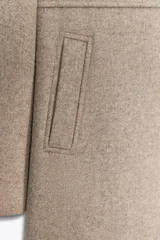 Abrigo color beige confeccionado en lana. Tiene cuello subido, mangas largas con hombreras, forro interior combinado y cierre frontal cruzado con botones metálicos.