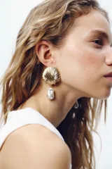 Aros colgantes dorados con forma de concha y perla irregular colgante.