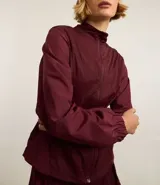 Campera deportiva rompevientos color bordó, con cuello alto, cierre frontal con cremallera, puños elastizados y recortes con hilo reflectante.