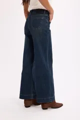 Pantalón de jean azul oscuro de tiro alto, con costuras verticales decorativas en el frente y cierre de botón metálico.