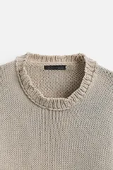 Jersey de punto color beige, de corte holgado, con cuello redondo y manga larga. Tiene efecto lavado y rotos en toda la prenda.