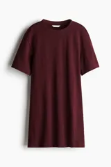 Vestido corto en punto de algodón suave color borgoña, con cuello redondo ribeteado acanalado, hombros caídos y mangas al codo. Pinzas moldeadoras en la parte posterior de la cintura para estilizar la figura.