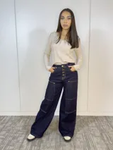 Pantalón de jean azul oscuro, de corte ancho, con bolsillos frontales y traseros, cierre frontal con botones dorados y costuras en color ocre.