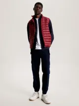 Chaleco acolchado rojo con cierre de cremallera, cuello alto y dos bolsillos laterales con cremallera. Tiene logo de Tommy Hilfiger bordado en el pecho.