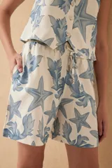 Short tipo bermuda de lino color crudo con estampado de estrellas de mar y hojas en color azul.
