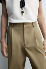Pantalón color caqui de corte tapered relaxed fit, confeccionado en tejido de algodón. Presenta cintura con pliegues frontales dobles, bolsillos laterales en cadera y bolsillos traseros de vivo con botón. Cierre frontal con cremallera y botón.