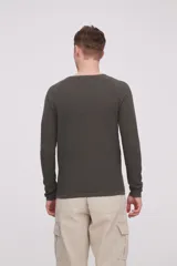 Sweater de algodón color verde oscuro, de manga larga y cuello redondo a la base. Presenta un tejido texturizado de punto fino.