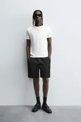 Bermuda negra de corte relajado, confeccionada en tejido satinado de viscosa. Presenta cintura elástica ajustable con cordón interior, bolsillos frontales y un bolsillo trasero de plastrón.